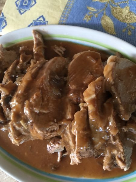 A large bowl with pork tenderloin and gravy in it sitting on table with a napkin under the bowl