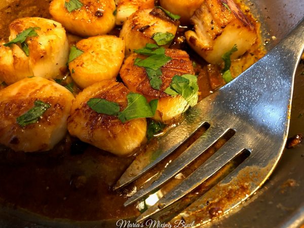 scallops in a pan with parsley on top and a large fork in pan