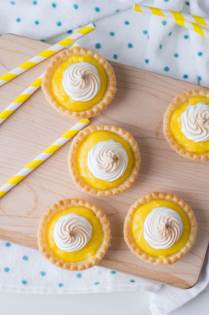 mini lemon pies on a cutting board with yellow straw by it, and topped with toasted meringue.