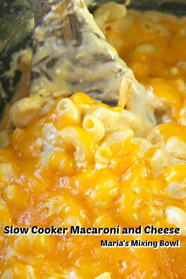  Macaroni and Cheese  in a slow cooker with a wooden spoon being stirred 