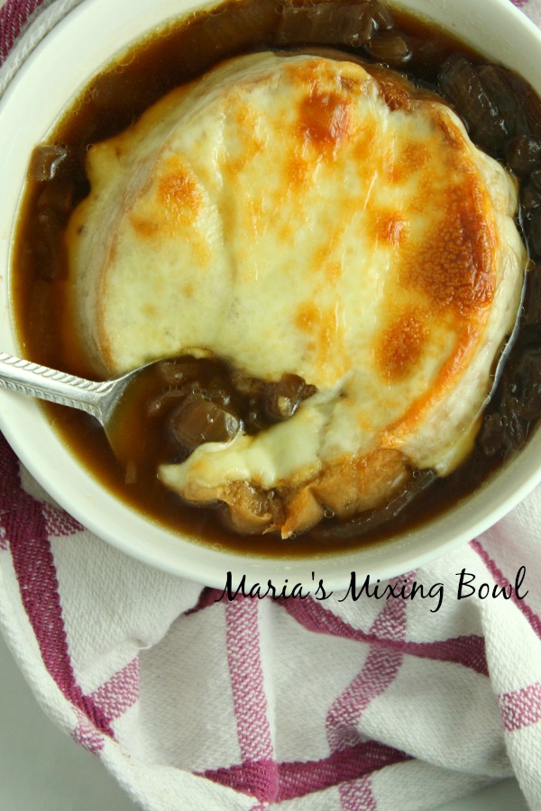 Spoon digging in to slow cooker French onion soup in white bowl.
