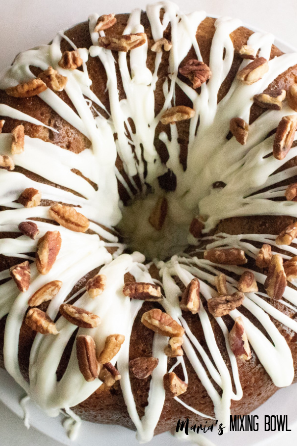 cake with frosting and pecans on a white plate with an overhead look of bundt cake 