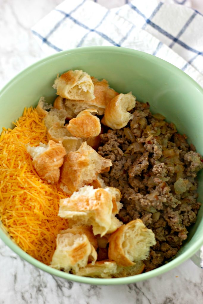 green bowl with cooked sausage, diced croissants, cheese, and onion in a bowl