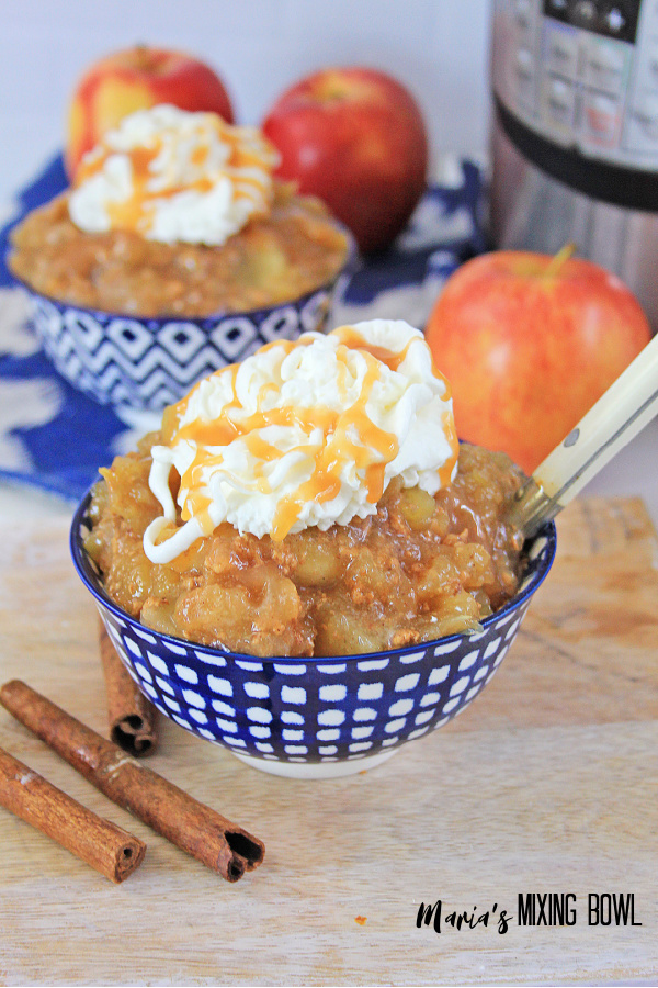 2 bowls of cinnamon apples cooked in the instant pot with whipped cream and caramel drizzle in blue and white bowls. Apples are place aroundthe bowls and the instant pot