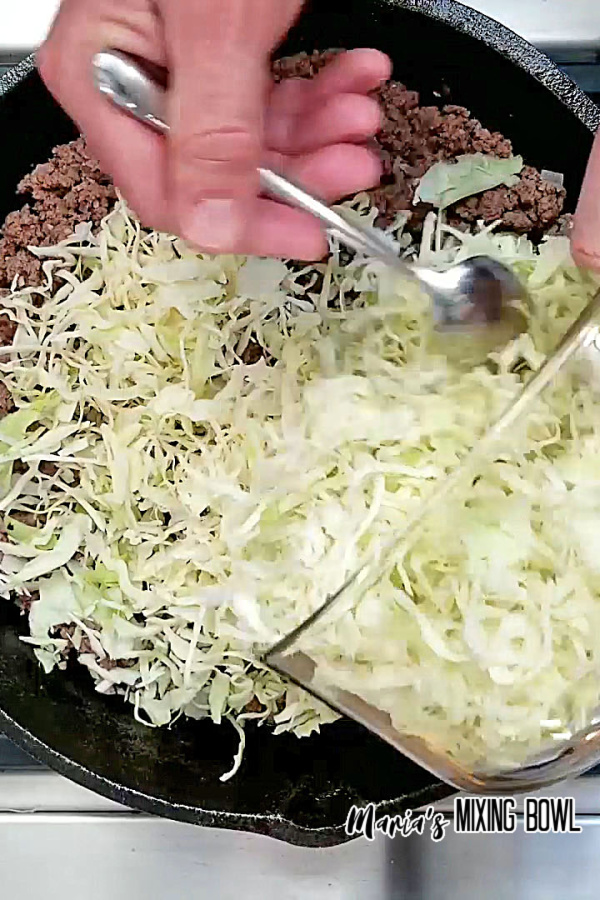 adding cabbage to ground beef in iron skillet on cooktop