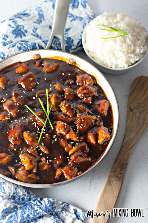 chicken in brown sauce with a bowl of white rice and blue and white napkin