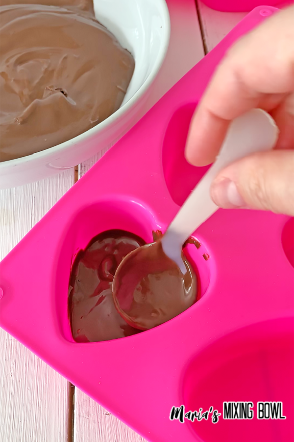 silicone heart mold being filled with chocolaate