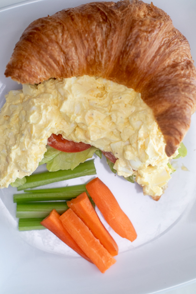 egg salad on a croissant with carrots and celery
