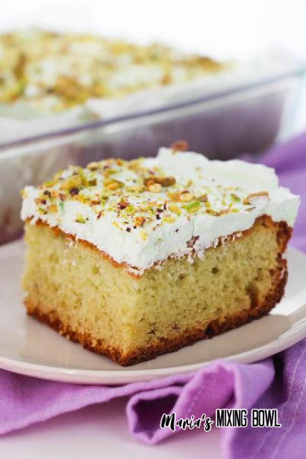 Slice of cake on white plate with baking dish full of more cake in background.