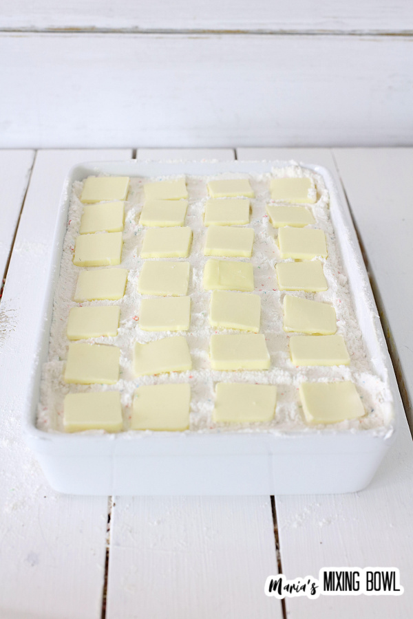 Dump cake topped with butter in white baking dish before baking