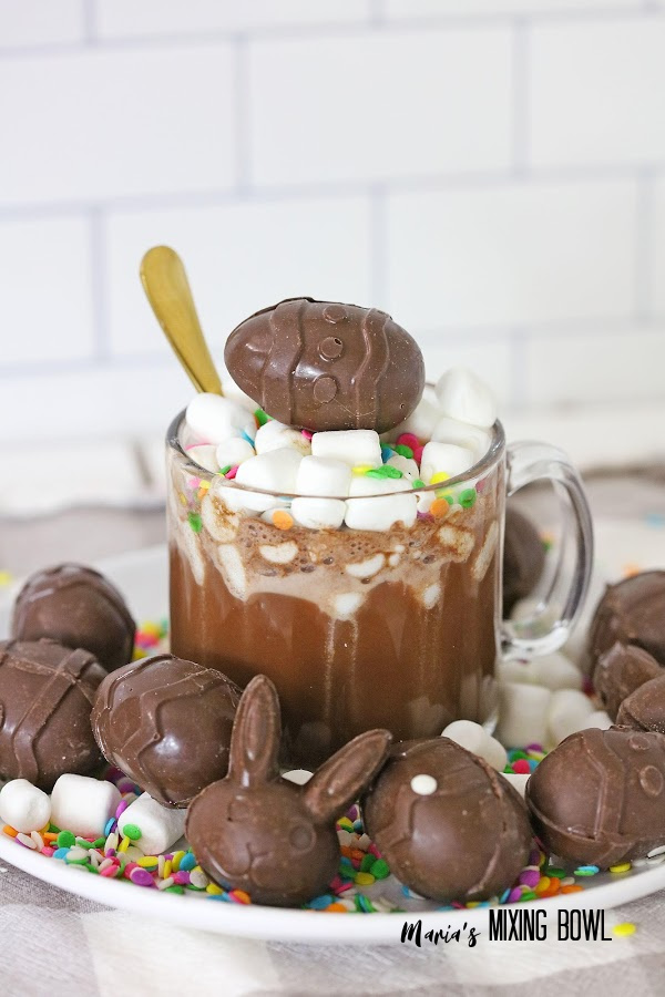 Egg and rabbit-shaped hot cocoa bombs surrounding glass mug filled with hot cocoa and topped with another bomb
