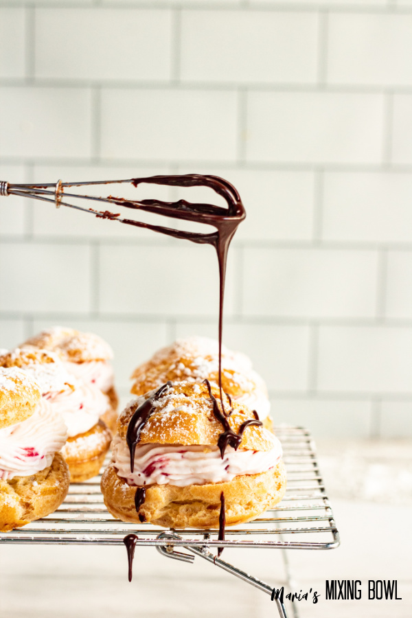 Wire wisk bineg used to drizzle chocolate over puff on wire rack