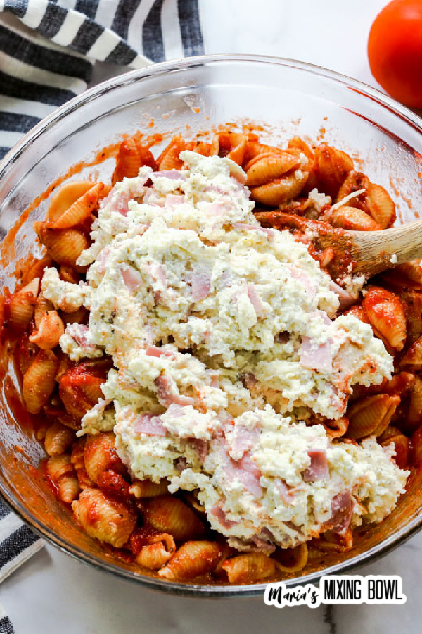 Mixing ham and cheese mixture into shells with sauce in glass bowl