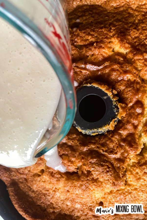 Liquid measuring cup drizzling glaze over bundt cake in pan