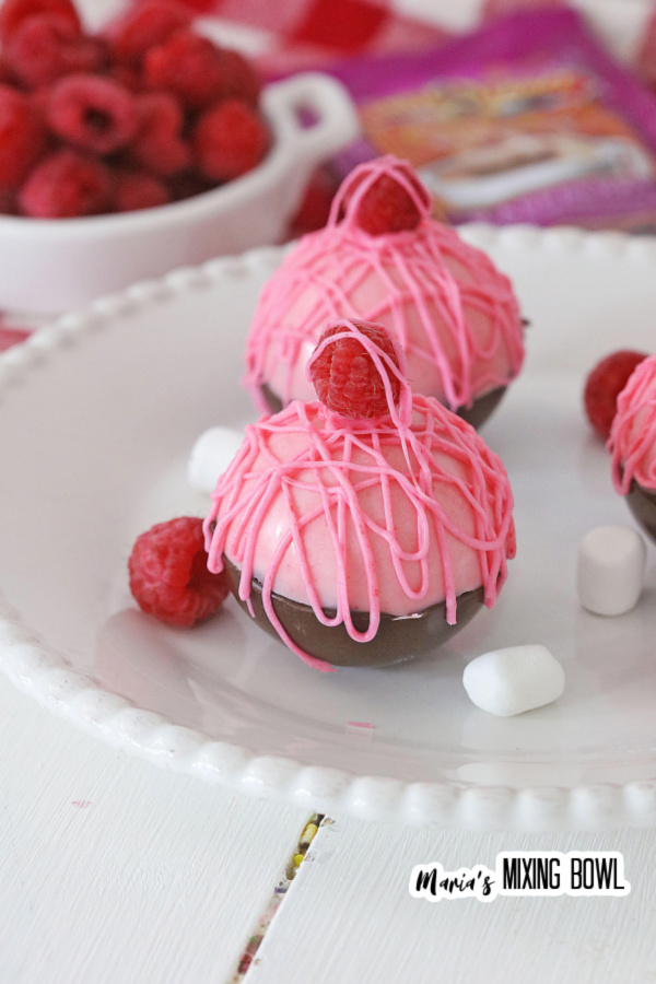 Closeup shot of white chocolate raspberry hot cocoa bombs with raspberries and mini marshmallows on plate