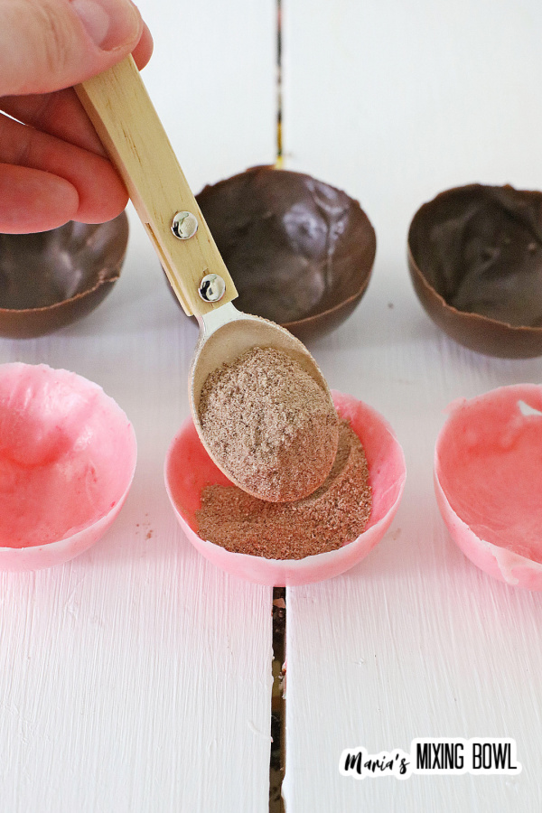 Spooning ingredients into pink shells for the cocoa bombs