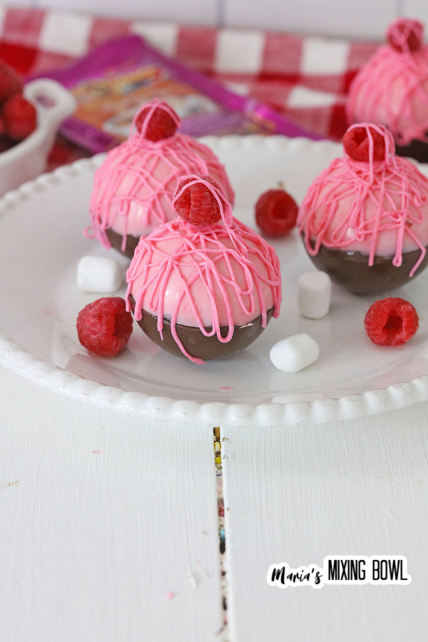 Closeup shot of hot chocolate bombs drizzled with pink chocolate and topped with a raspberry on plate