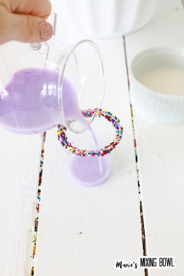 Pouring purple birthday cake shot into glass with sprinkled rim