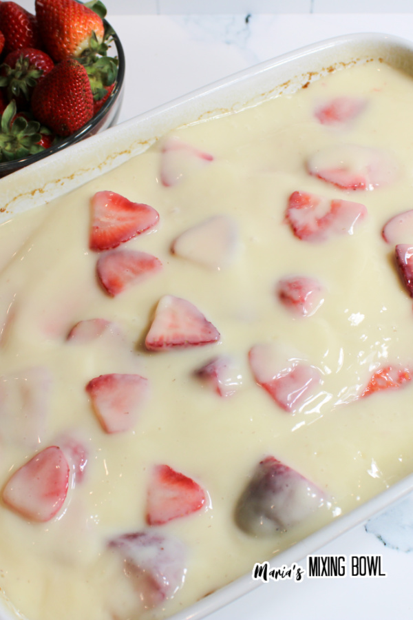 Cake topped with pudding and strawberries in baking dish