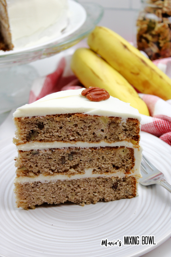 Slice of hummingbird cake on white plate with bananas in background