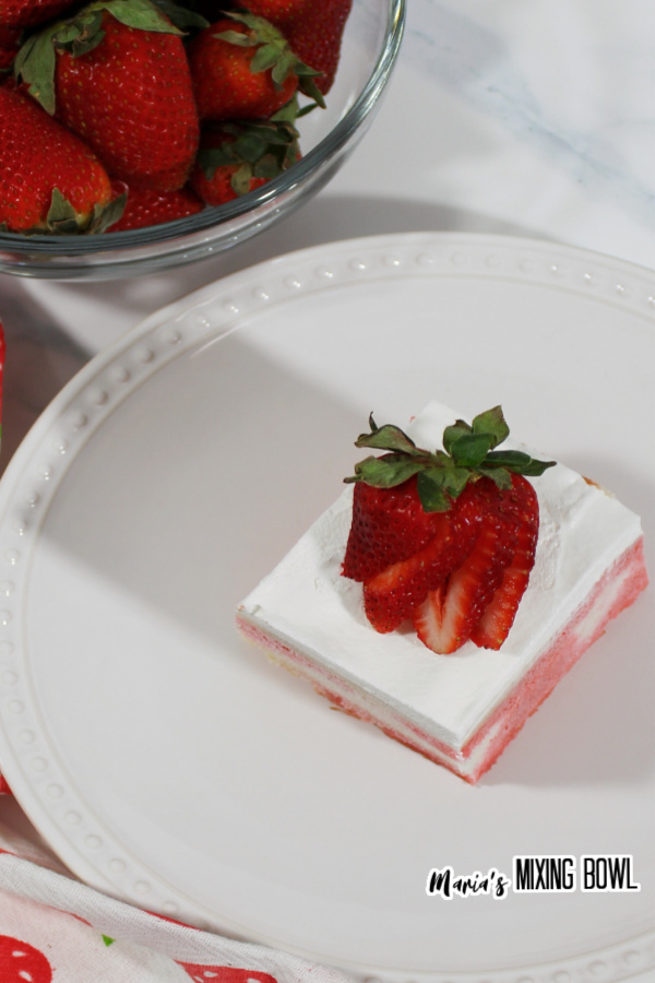 Overhead shot of strawberry cheesecake poke cake on white plate