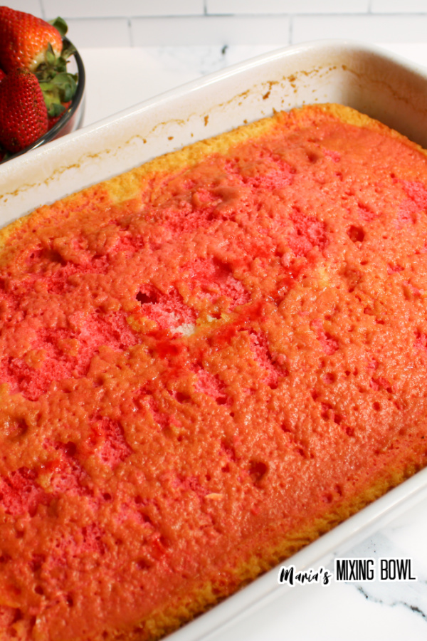 Cake in baking dish with holes poked in it and soaked in strawberry Jello