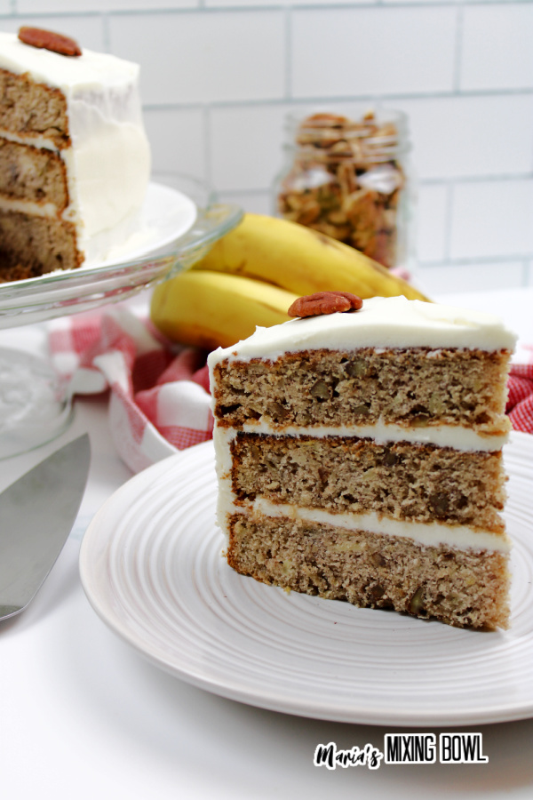 Slice of hummingbird cake on plate with more cake on cake stand in background