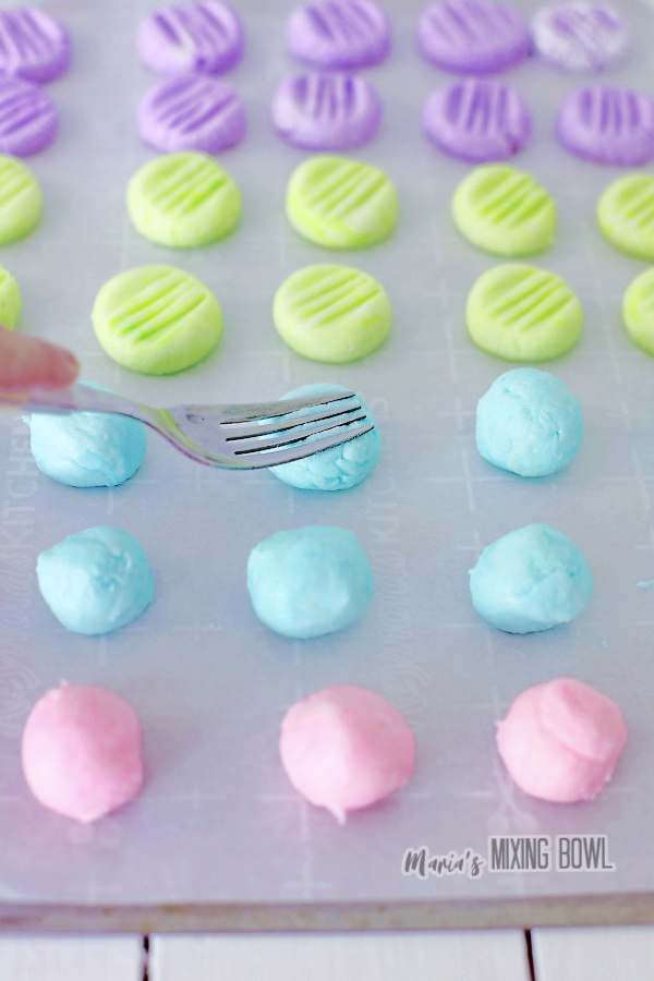 Fork pressing down cream cheese mints on parchment paper-lined baking sheet
