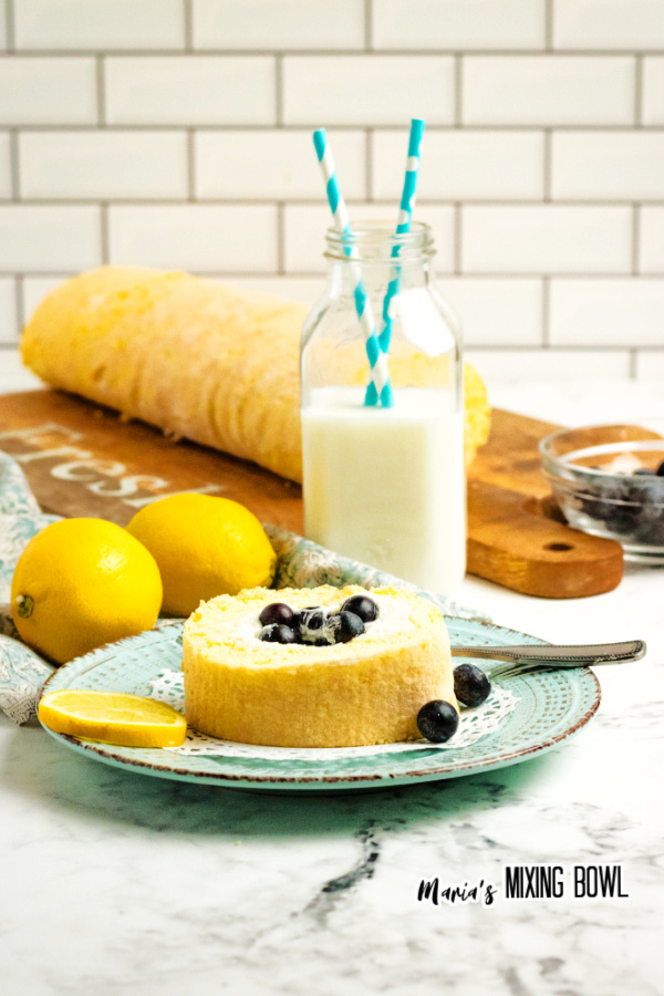 Slice of lemon blueberry cake roll on plate with glass of milk in background