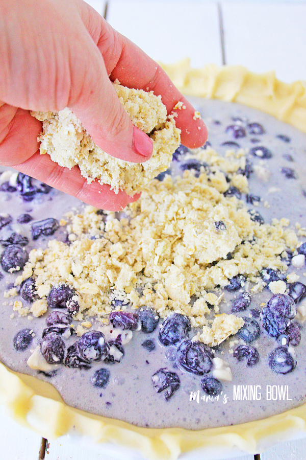 Closeup shot of hand sprinkling muffin topping over blueberry cheesecake mixture