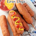 Overhead shot of homemade corn dog with bowl of ketchup and mustard on plate