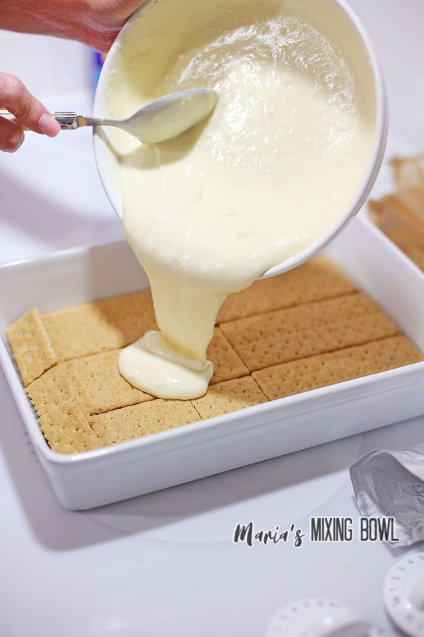 Batter being poured from a bowl over graham crackers in baking dish