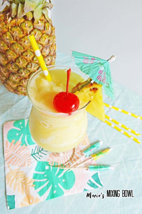 cherry and pineapple, umbrella atop a pina colada with pineapple in background