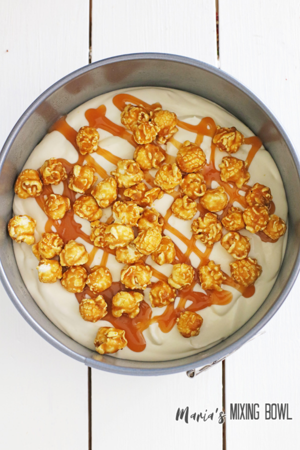 Cheesecake batter topped with caramel corn and caramel sauce in springform pan