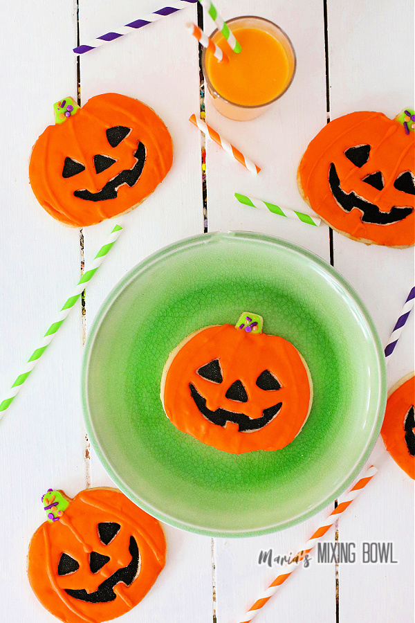 Overhead shot of jack-o-lantern cookies surrounding plate with another cookie