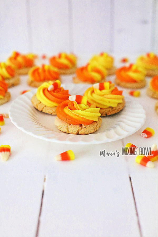 Candy corn cookies on white plate with more cookies in background.