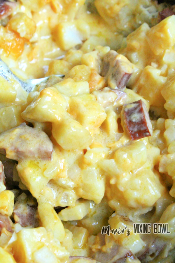 Closeup shot of spoon sitting in cheesy kielbasa hashbrown casserole