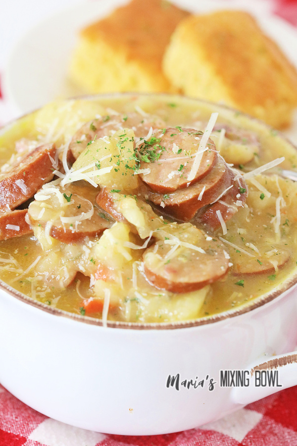 Closeup shot of bowlful of kielbasa potato soup with plate of cornbread in background