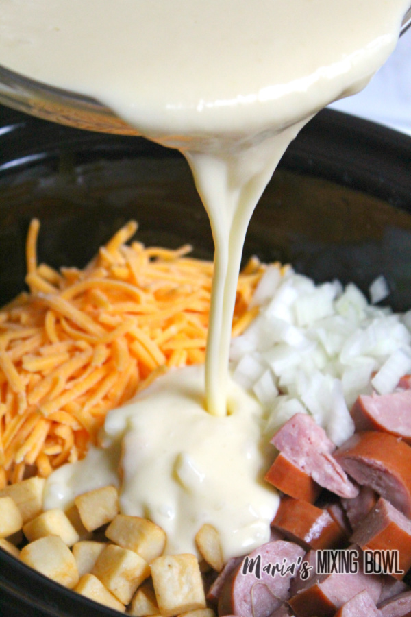 Pouring cream mixture from a bowl over casserole ingredients in slow cooker