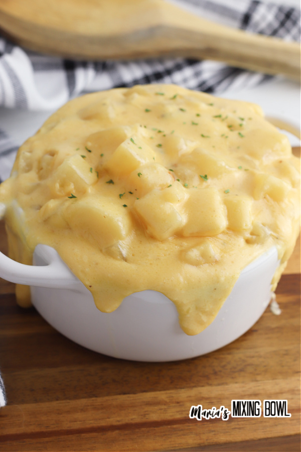 slow cooker cheesy potatoes recipe in a white crock on a wood board