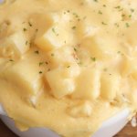 slow cooker cheesy potatoes recipe in a white crock on a wood board