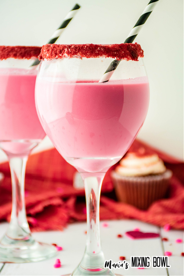 Two glasses of red velvet cocktial with cupcakes in background