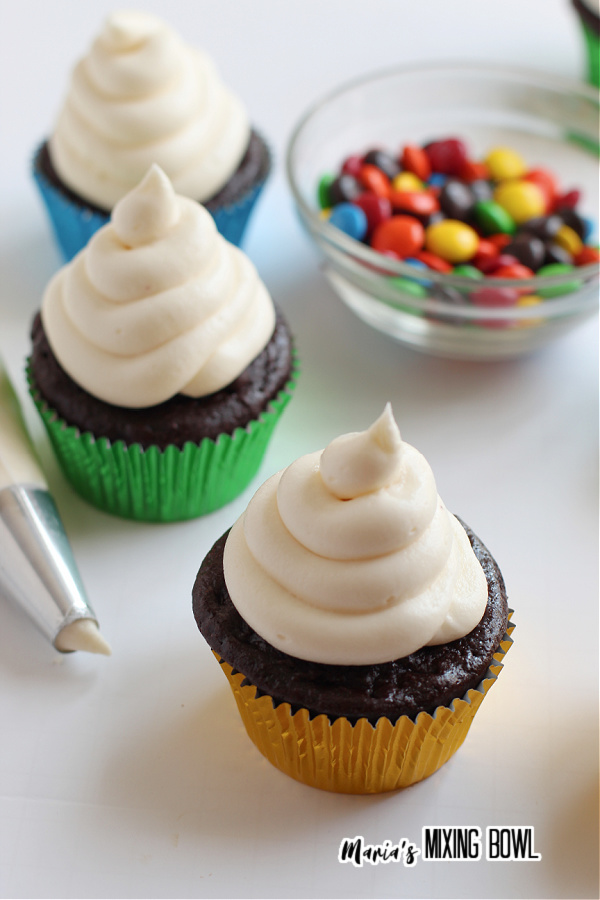 Frosted chocolate cupcakes with bowl of M&Ms in background