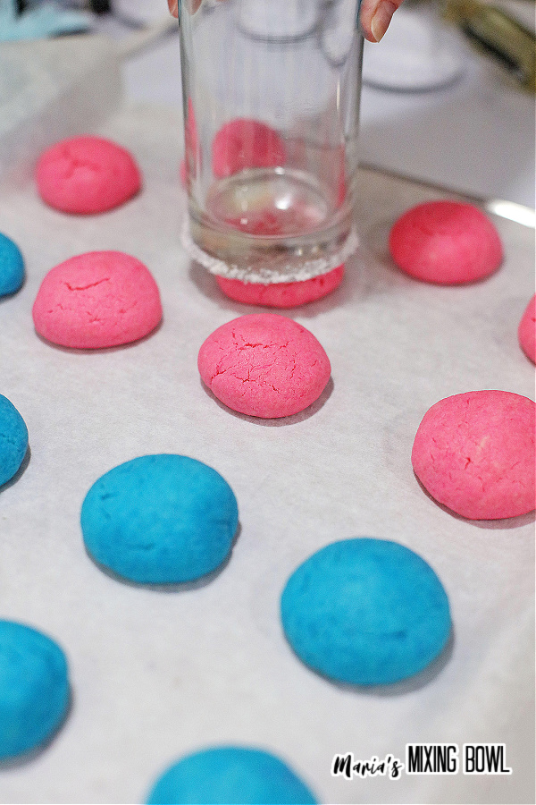 Glass being used to press blue and pink cookie dough down