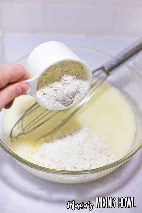 Flour being poured into wet waffle ingredients.