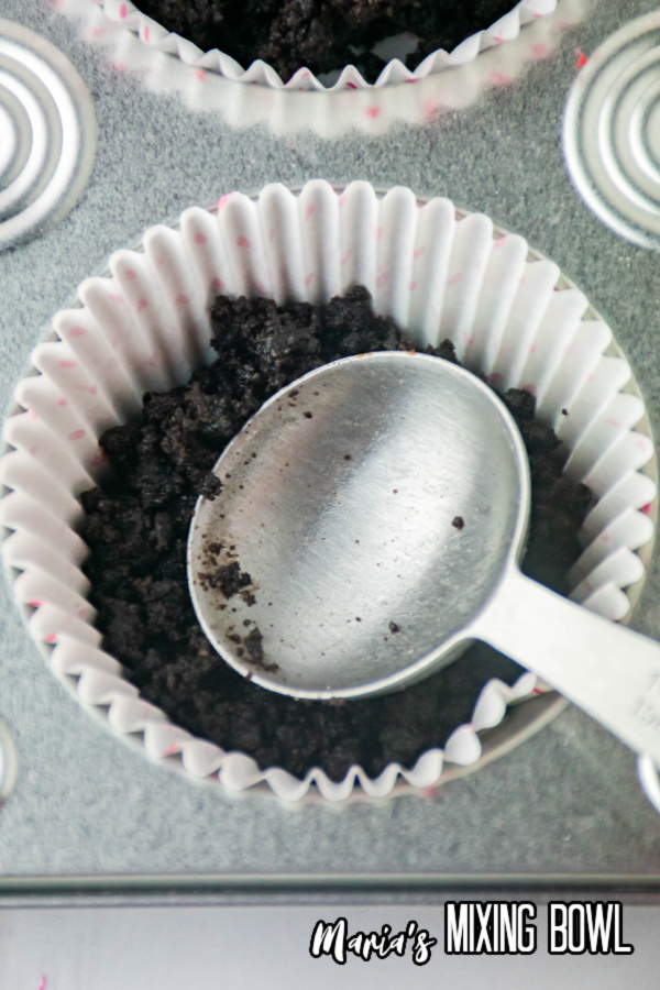 Overhead shot of spoon pressing oreo crumbs into bottom of muffin cup