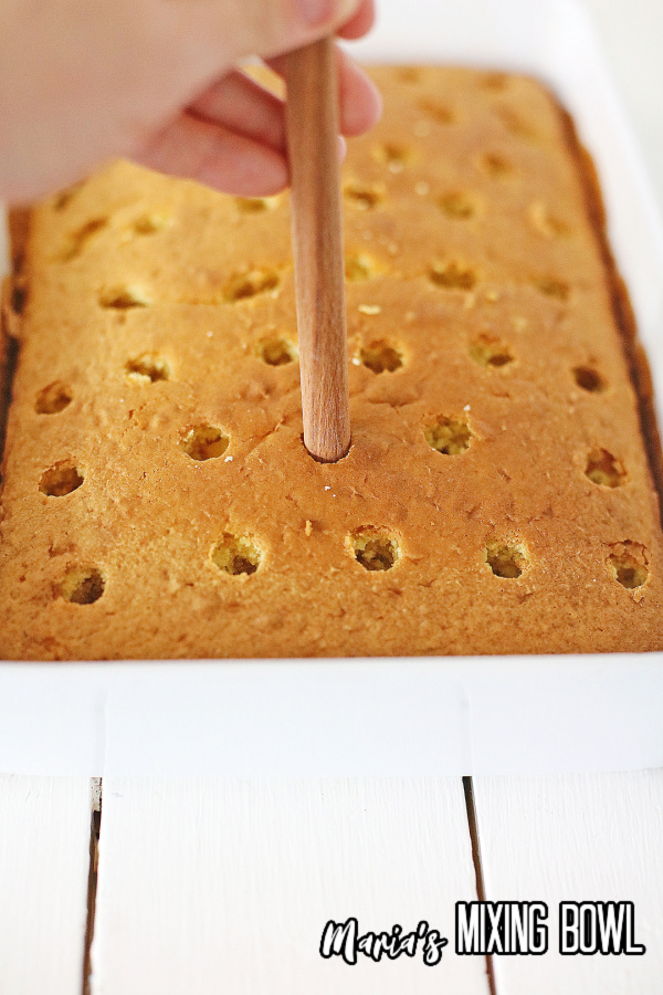 Wooden spoon handle being used to poke holes in cake in baking dish
