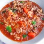 Cabbage Roll Soup in white bowl, bread and spoon and purple and white napkin