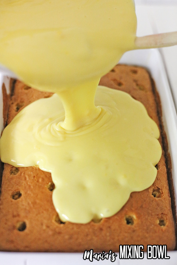 Vanilla pudding being poured over cake with holes poked in it