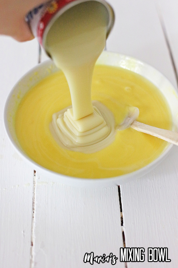 Sweetened condensed milk being poured into bowl of vanilla pudding